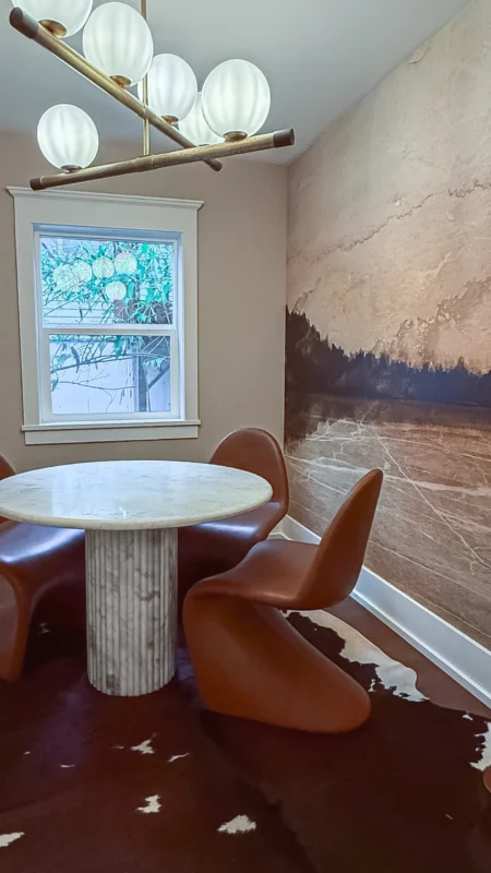 Small meeting room corner featuring a round marble table, brown leather-look chairs, and a feature wall with a large, abstract mural that resembles a landscape.