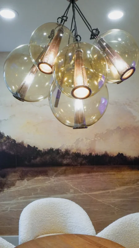 Close-up of a multi-globe amber glass chandelier hanging above a meeting area with wallpaper depicting an abstract landscape.