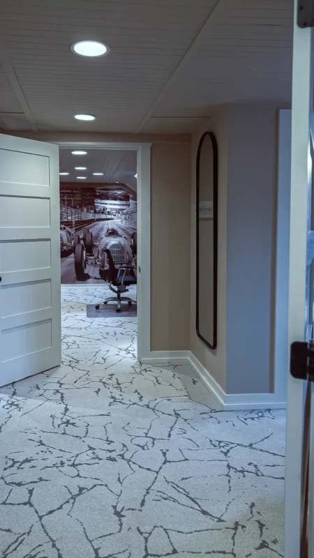 Vertical shot of a hallway with white paneled doors, white trim, and a white-patterned carpet, leading into a room with a large black-and-white wall mural of a vintage race car.