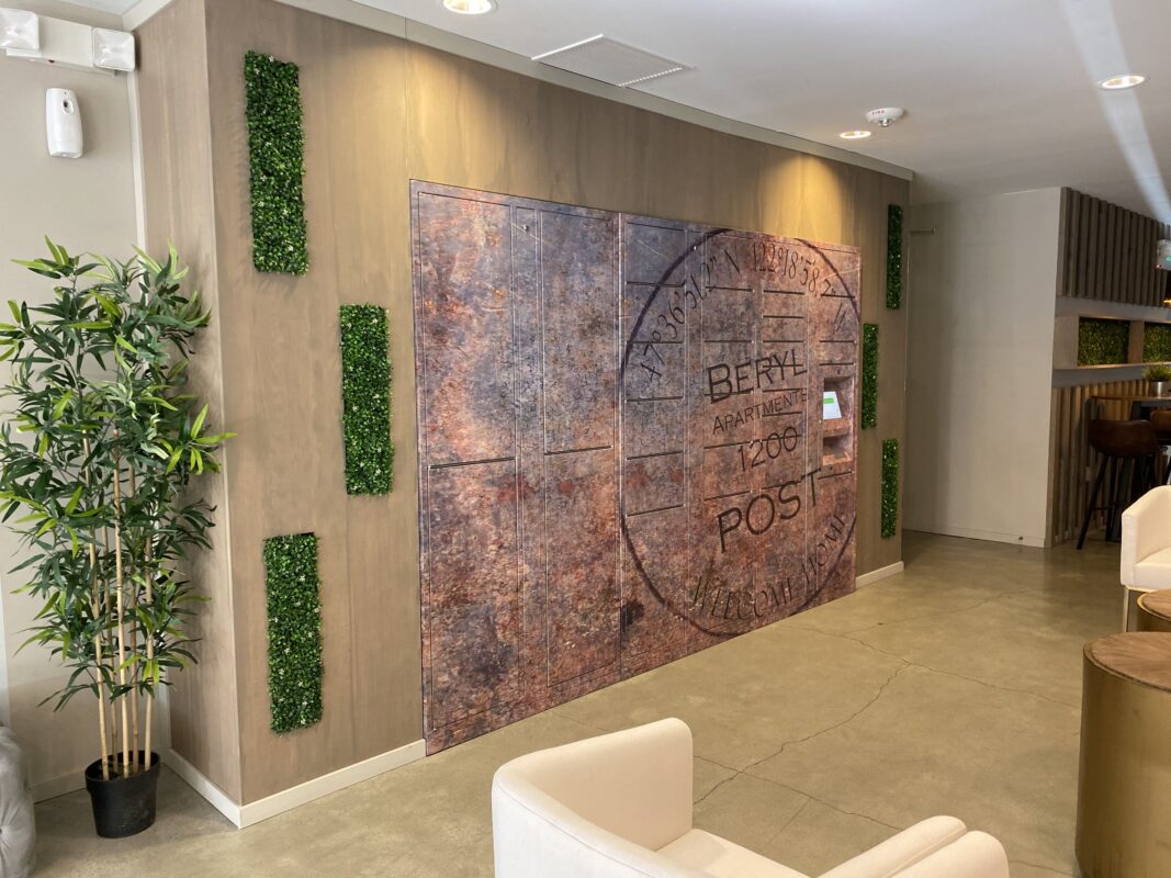 Apartment lobby with blue abstract mural, tufted bench seating and greenery leading toward lounge area.