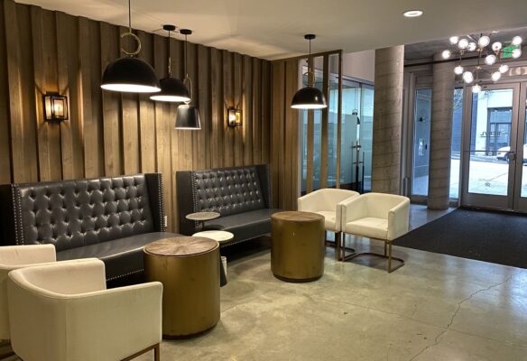 Modern apartment lounge with tufted grey sofas, white chairs and gold drum tables against vertical wood slat wall.