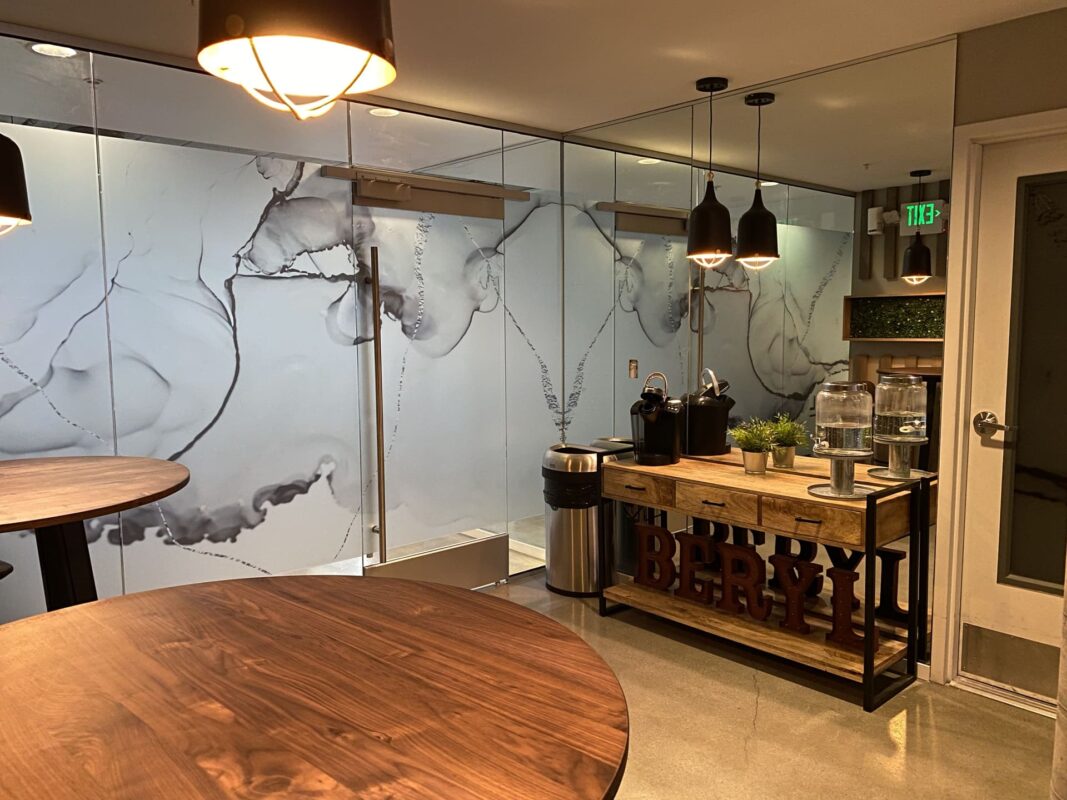 Lounge refreshment station with Keurig, glass water dispensers and decorative BERYL letters beneath console.