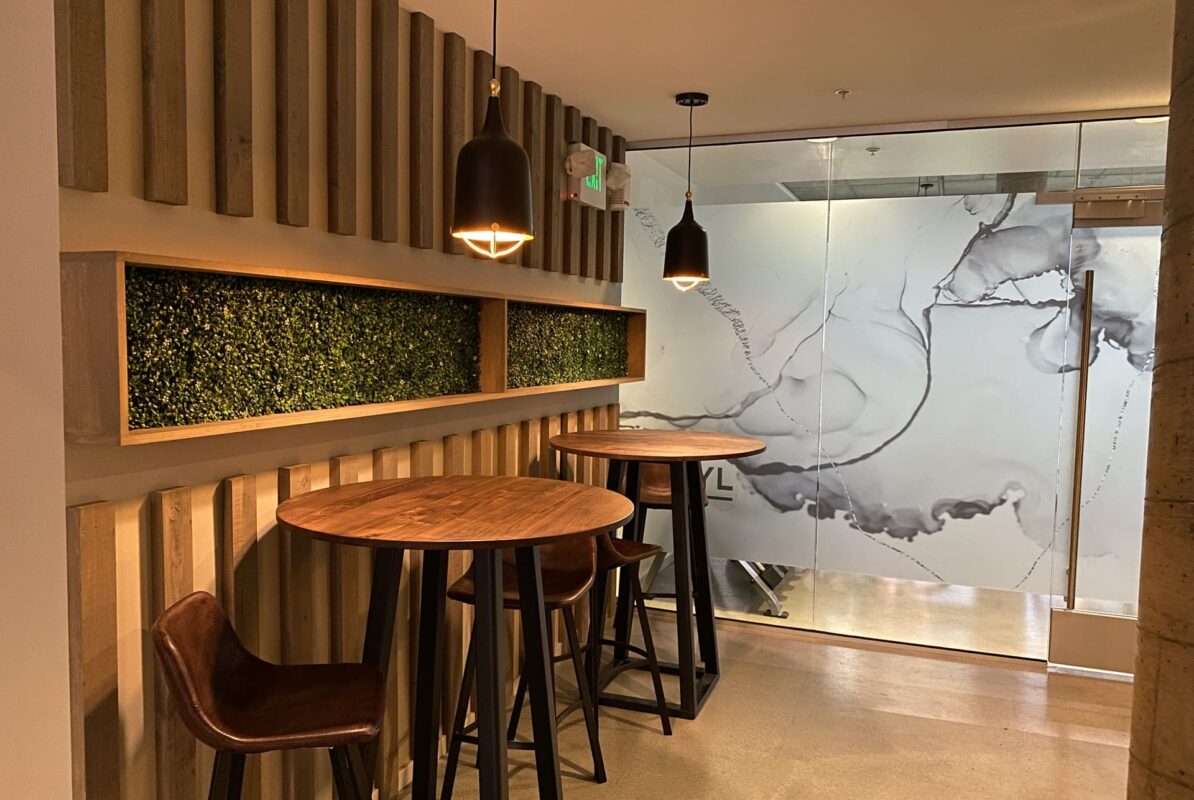 Group seating arrangement with tufted sofas, white armchairs and round metallic tables on polished concrete floor.