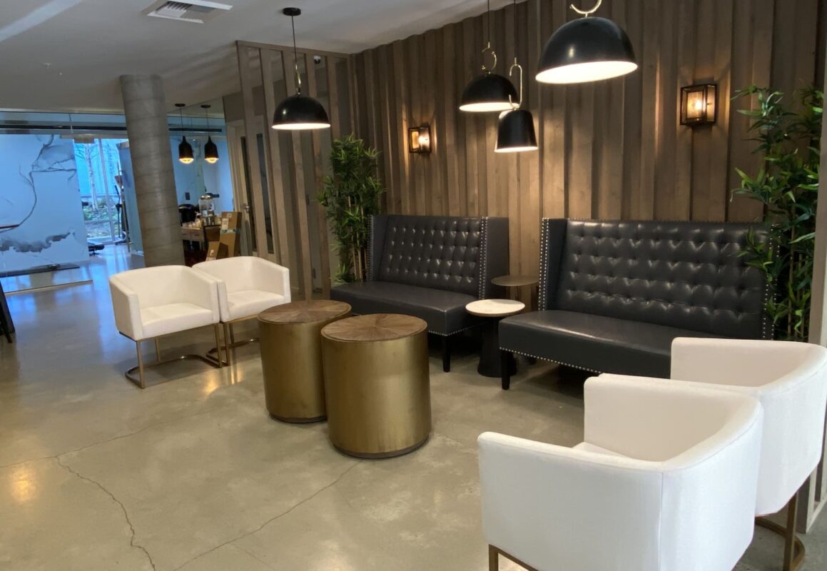 Dual high‑back tufted sofas facing gold drum tables and white chairs in lobby lounge.
