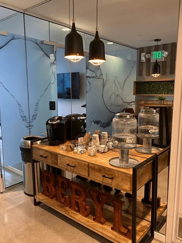 Wood and metal sideboard with coffee setup, plants and black pendants in front of mirrored wall.