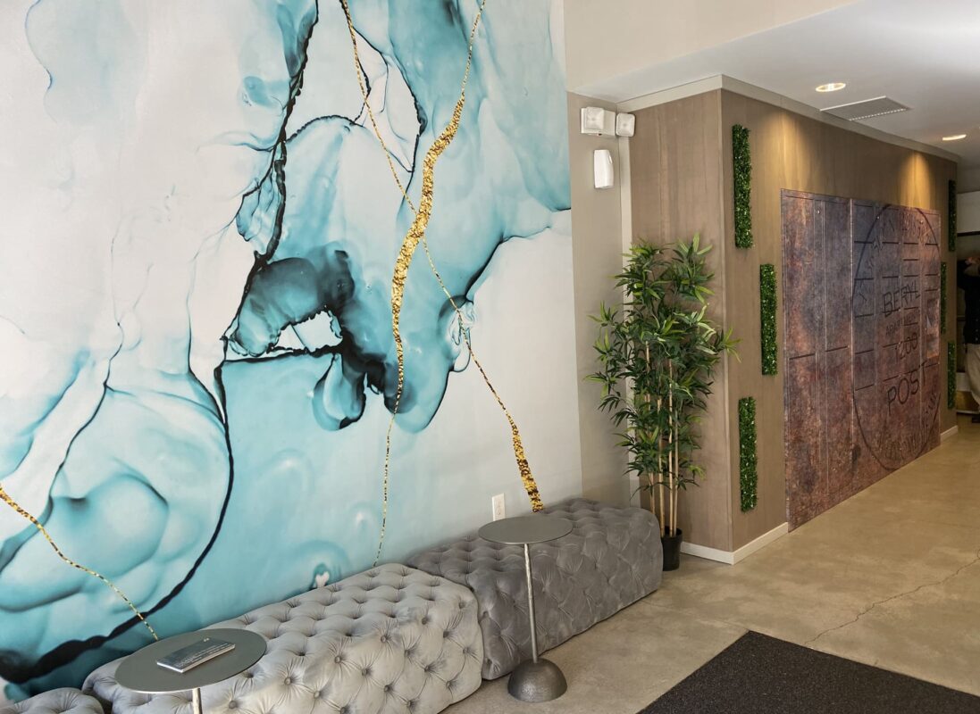 Large-scale aqua and gold abstract wall art above tufted grey bench seating in lobby.
