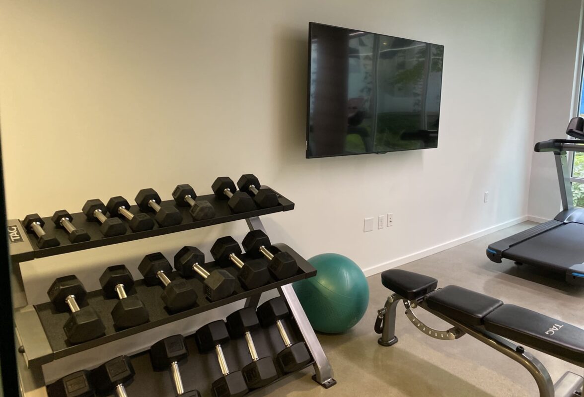 Gym corner showing glass wall with frosted abstract pattern and double-tier dumbbell rack.