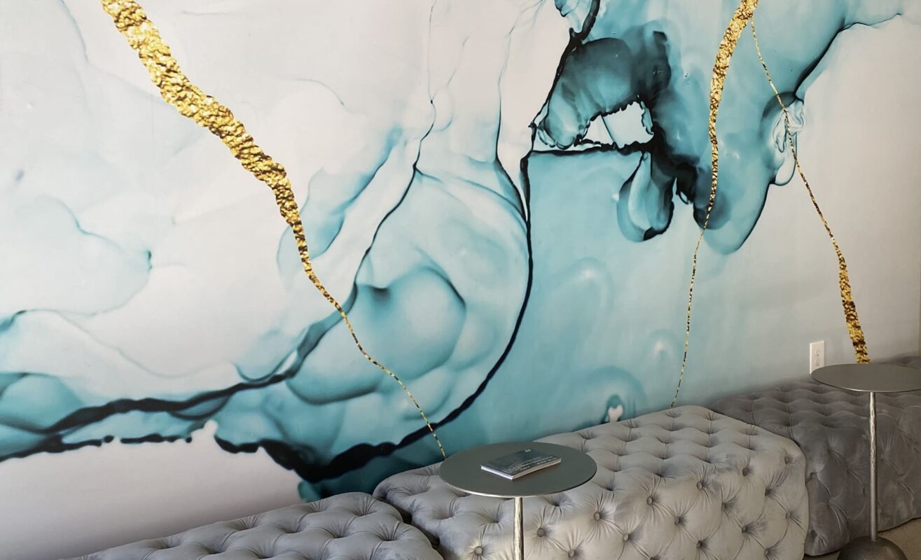 Large-scale aqua and gold abstract wall art above tufted grey bench seating in lobby.