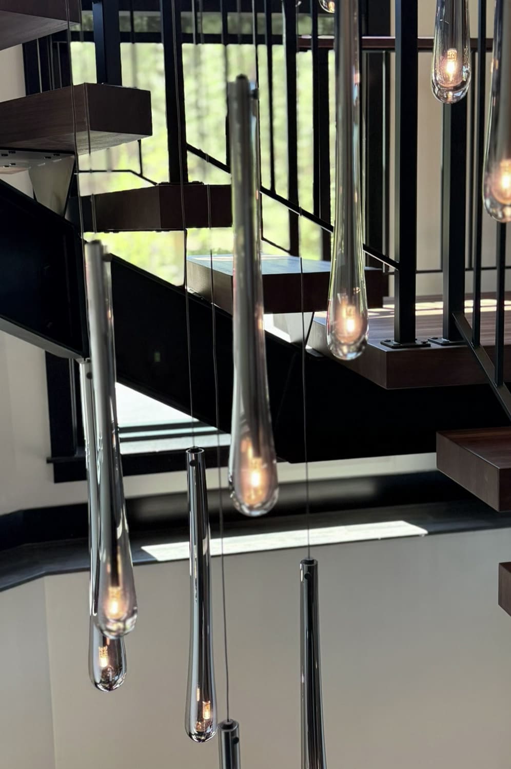 Close up of amber teardrop glass pendants beneath the floating wood treads and black steel railings of the Suncadia home staircase.