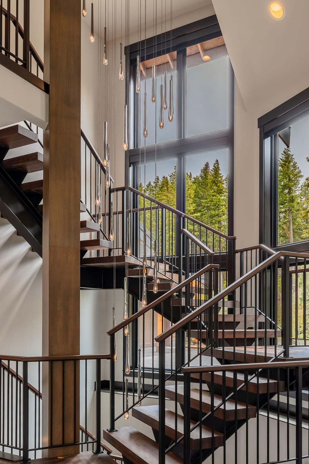 Full view of the two story Suncadia staircase with floating wood treads, black metal railings, wood accent column, and the teardrop pendant cascade falling through the stairwell.