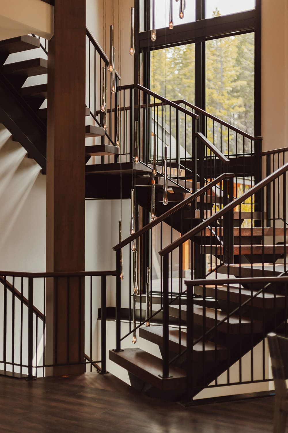Side elevation of the Suncadia home staircase showing the switchback design, floating wood treads, black railings, and vertical pendant cascade against the landing window.