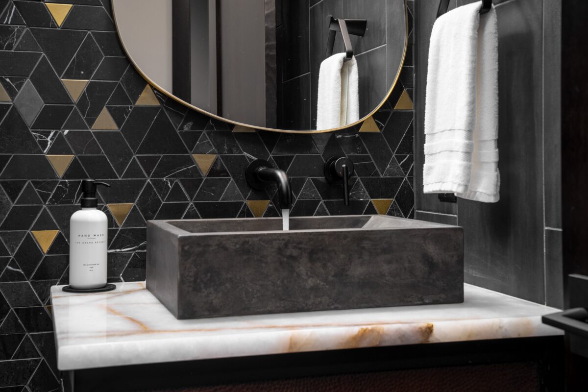 Luxury powder room in a Suncadia home with black and brass triangular mosaic tile, organic brass framed mirror, and concrete vessel sink on a white onyx vanity.
