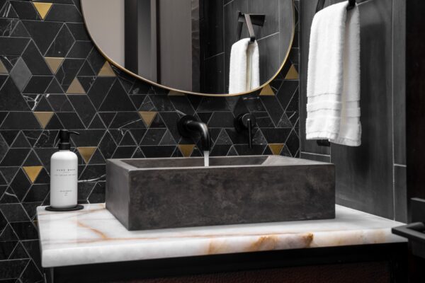 Luxury powder room in a Suncadia home with black and brass triangular mosaic tile, organic brass framed mirror, and concrete vessel sink on a white onyx vanity.