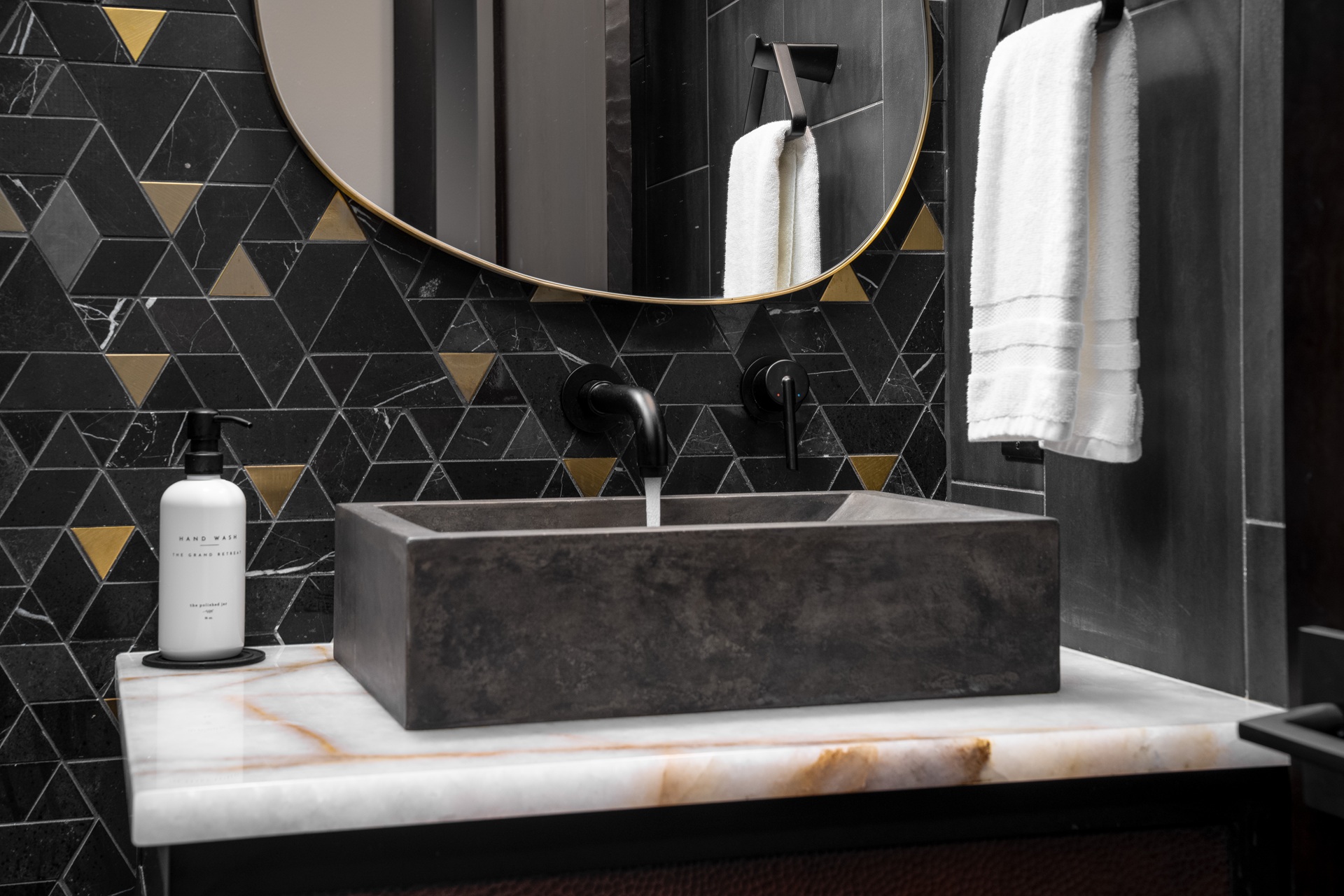 Luxury powder room in a Suncadia home with black and brass triangular mosaic tile, organic brass framed mirror, and concrete vessel sink on a white onyx vanity.